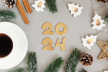 Cup of coffee spruce twigs numbers 2024 and garland on gray textured table. Idea template for...