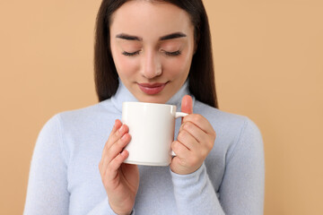 Beautiful young woman holding white ceramic mug on beige background