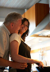 Mature couple, embrace and cooking together with food, love and marriage at stove in home for lunch. Happiness, old man and woman in kitchen with hug, smile and meal prep for dinner in apartment.