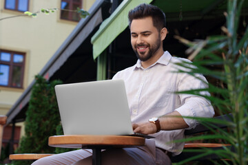 Handsome young man working on laptop at table in outdoor cafe