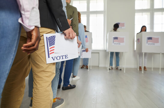 Diverse citizens at ballot station on election day. White and African American male and female voters holding voting forms in hands standing in line at polling place. Crop shot. US democracy concept 