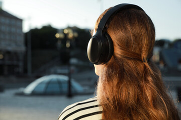 Woman in headphones listening to music on city street, back view. Space for text