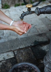 A woman washes her hands under an old tap on the street. Old part of the city.