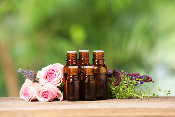 Bottles with essential oils, herbs and flowers on wooden table against blurred green background....