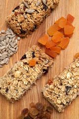 Different tasty granola bars and ingredients on wooden table, flat lay