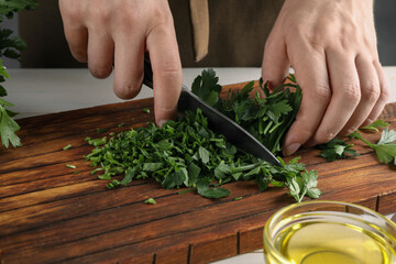 Woman cutting fresh parsley at white table, closeup