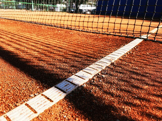 Detailed view of outdoor tennis clay court with white lines, net and shadows. Traditional outdoor sports arena. Fitness and training backgrounds