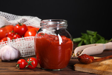 Jar of tasty tomato paste and ingredients on wooden table