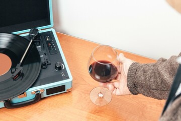 Horizontal photo senior adult hand holding glass of wine next to record player Concept hobbies art