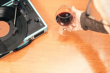 Horizontal photo senior adult hand holding glass of wine next to record player Concept hobbies art
