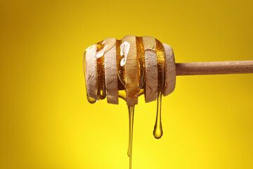 Delicious honey flowing down from dipper against yellow background, closeup
