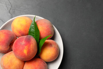 Fresh peaches and leaves in bowl on grey textured table, top view. Space for text