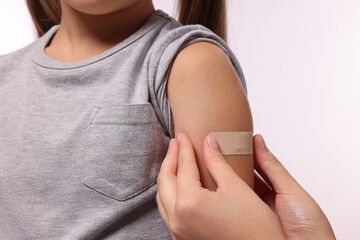 Woman sticking plaster on girl's arm after vaccination against white background, closeup