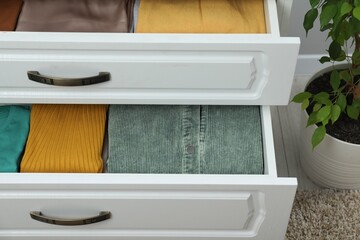 Sorting and organizing. Chest of drawers with different folded clothes indoors