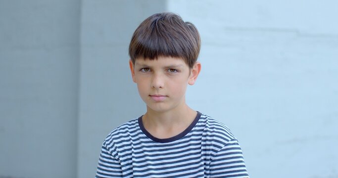 Young boy in striped shirt making direct eye contact with the camera. Use of natural lighting suggests soft and authentic quality of visual image. Intimate and engaging lifestyle portrait of teenager.