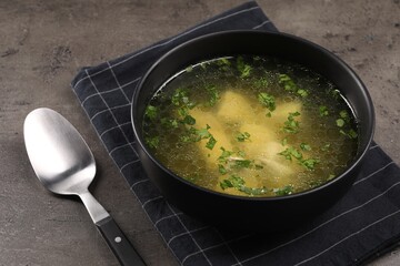 Delicious chicken soup with parsley and spoon on grey table, closeup