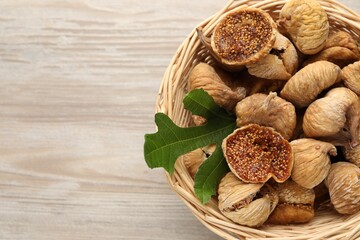 Wicker basket with tasty dried figs and green leaf on light wooden table, top view. Space for text