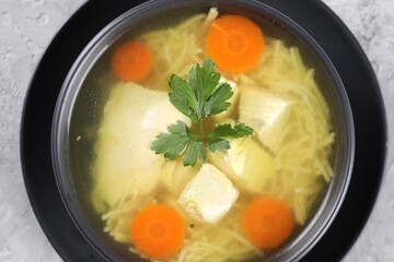 Tasty chicken soup with noodles, carrot and parsley in bowl on light textured table, top view