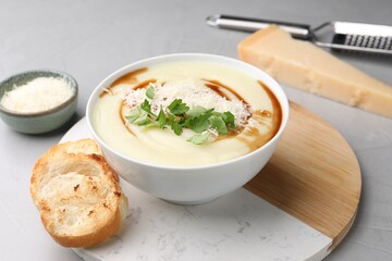 Delicious cream soup with parmesan cheese, soy sauce in bowl and croutons on light grey table