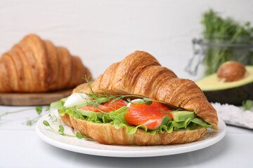 Tasty croissant with salmon, avocado, mozzarella and lettuce on white table, closeup