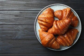 Delicious fresh croissants on black wooden table, top view. Space for text