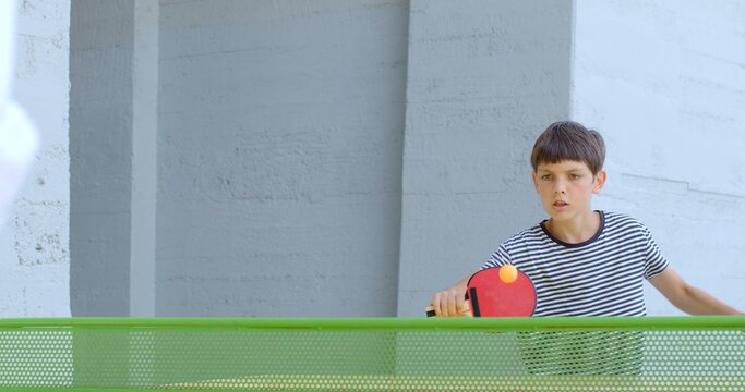 Boy playing table tennis in the park. Find suitable playing area, set up the equipment, enjoy quality time together while staying active and healthy. Teens transition from childhood to adulthood.