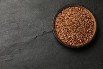 Bowl with dry buckwheat on black table, top view. Space for text