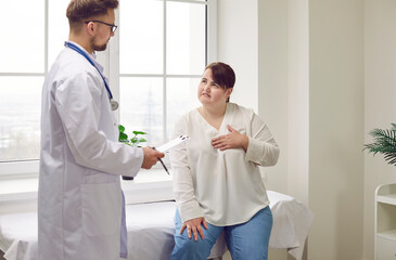 Young fat woman sitting on the couch in the doctor's office and pointing to her chest to the doctor...