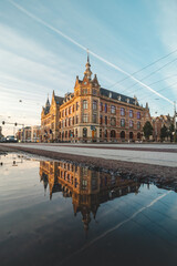 Fototapeta premium Historic building in the centre of Amsterdam under the light from the sunset at a busy intersection in the middle of the city with a reflection in a puddle