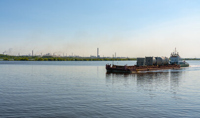 Fototapeta na wymiar A barge carries cargo along the Sheksna River against the backdrop of the Cherepovets Metallurgical Plant