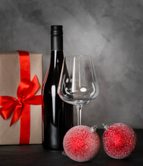 Wine bottle with glass and red Christmas balls on a dark background