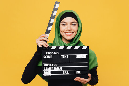 Young arabian asian muslim woman wear green hijab abaya black clothes hold classic black film making clapperboard isolated on plain yellow background People uae middle eastern islam religious concept