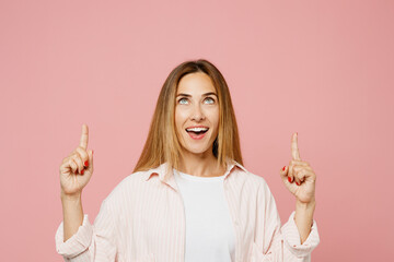 Young surprised amazed fun woman wear shirt white t-shirt casual clothes point index finger overhead on area mockup isolated on plain pastel light pink background studio portrait. Lifestyle concept.