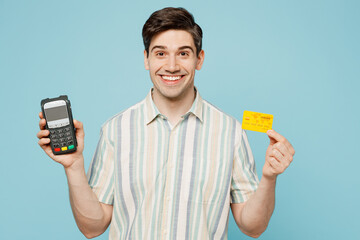 Young happy man he wears striped shirt casual clothes hold wireless modern bank payment terminal to process acquire credit card isolated on plain pastel light blue cyan background. Lifestyle concept.
