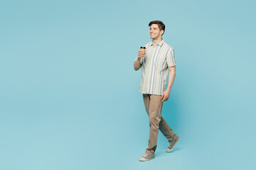 Full body side view young happy man he wears striped shirt casual clothes hold takeaway delivery craft paper brown cup coffee to go isolated on plain pastel light blue cyan background studio portrait.