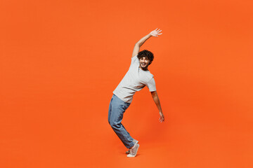 Full body side view young smiling happy Indian man he wears t-shirt casual clothes stand on toes leaning back with outstretched hands isolated on orange red color background studio. Lifestyle concept. - obrazy, fototapety, plakaty