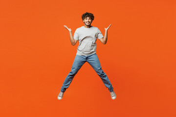 Fototapeta na wymiar Full body young overjoyed excited smiling happy Indian man he wears t-shirt casual clothes jump high spread hands look camera isolated on orange red color background studio portrait Lifestyle concept