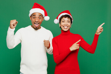 Merry young couple friends man woman wear red casual clothes Santa hat posing point index finger...