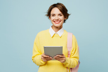 Young happy fun cool woman IT student wear casual clothes yellow sweater backpack bag hold in hand digital tablet pc computer isolated on plain blue background High school university college concept.