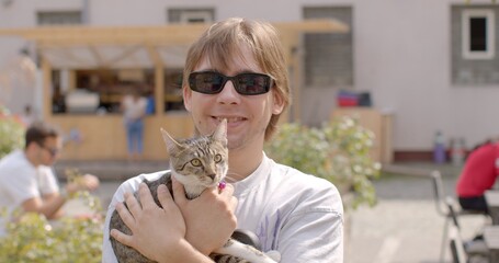 Portrait of young man holding cat against backdrop of urban environment. Unique bond between humans and pets, moments of genuine connection and solace. deep connection shares with four-legged friend.