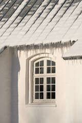 Empty building with ice damming on the roof on a cold winter day. The exterior of a home or house with snow on the rooftop on a sunny afternoon. Frost on a historic church in a village