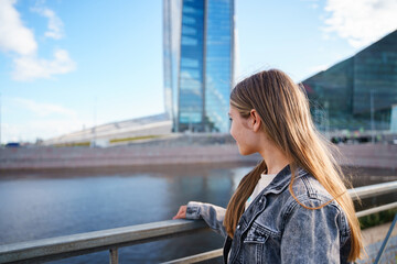 A teenage girl walks next to a high business tower in St. Petersburg - obrazy, fototapety, plakaty