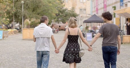 Girl and two guys, back view. Urban environment. Romantic relationships among three individuals...