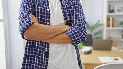 Confident young arab man asserts his success in business world, standing with crossed arms in office, exuding professionalism