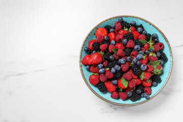 Many different fresh ripe berries in bowl on white table, top view. Space for text