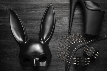 Black rabbit mask, studded leather bracelets and neck choker on the black wooden table background.