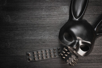 Black rabbit mask and studded leather bracelets on the black wooden table background with copy...