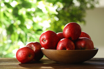 Ripe red apples and bowl on wooden table outdoors