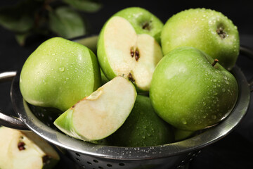 Ripe green apples with water drops in colander on table, closeup