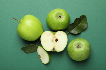Whole, cut green apples and leaves on color background, flat lay